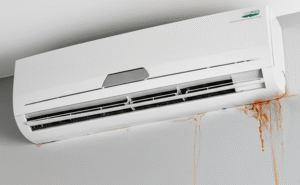 A visibly dirty wall and a small puddle of water on the floor, indicating a leak from an A/C system.