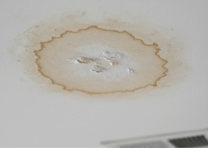 A noticeable light brown water stain on a ceiling near an air vent, illustrating an A/C drain line leak.