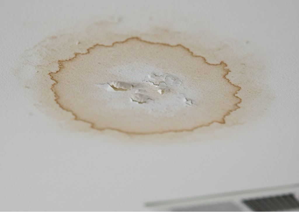 A noticeable light brown water stain on a ceiling near an air vent, illustrating an A/C drain line leak.